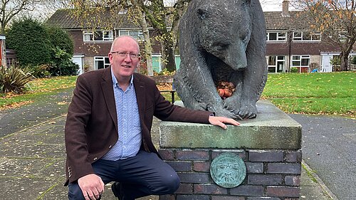Cllr Fenton kneeling by the Chalfonts Bear plinth, with its newly reinstated plaque