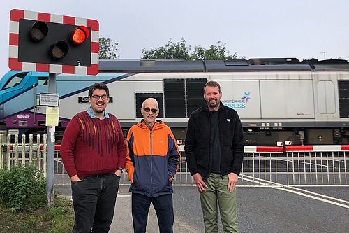 Councillors Pearson, Cuthbertson and Hollyer standing in front of a level crossing as a Transpennine Nova 3 passes behind them